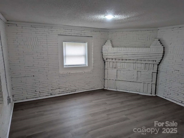 unfurnished room featuring brick wall, a textured ceiling, and wood finished floors