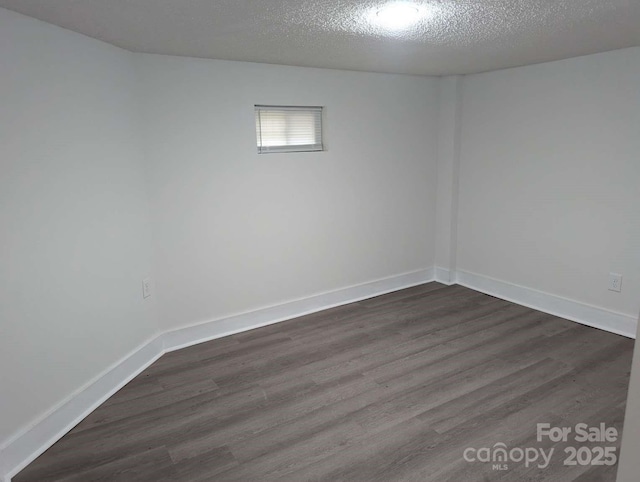 unfurnished room with a textured ceiling, dark wood-type flooring, and baseboards