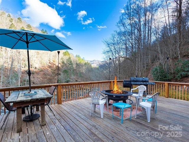 deck featuring area for grilling, a fire pit, and a view of trees