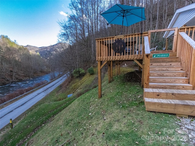 wooden deck with a forest view, a lawn, and stairway