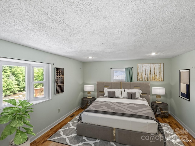 bedroom with multiple windows, wood finished floors, and baseboards