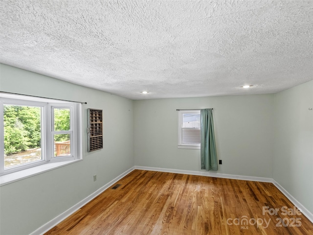 unfurnished room with visible vents, wood finished floors, baseboards, and a textured ceiling