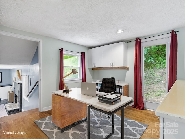 office space featuring a fireplace, light wood-type flooring, and a textured ceiling