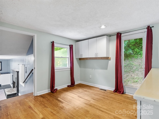 kitchen with visible vents, light wood-style flooring, light countertops, white cabinets, and a textured ceiling