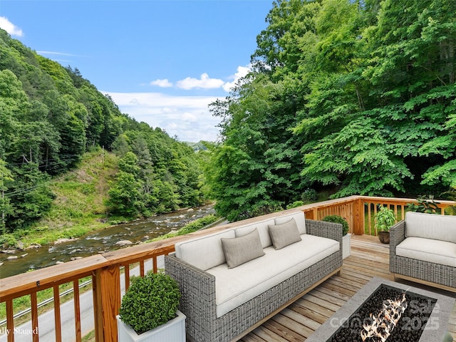 wooden deck featuring an outdoor living space with a fire pit, a wooded view, and a water view