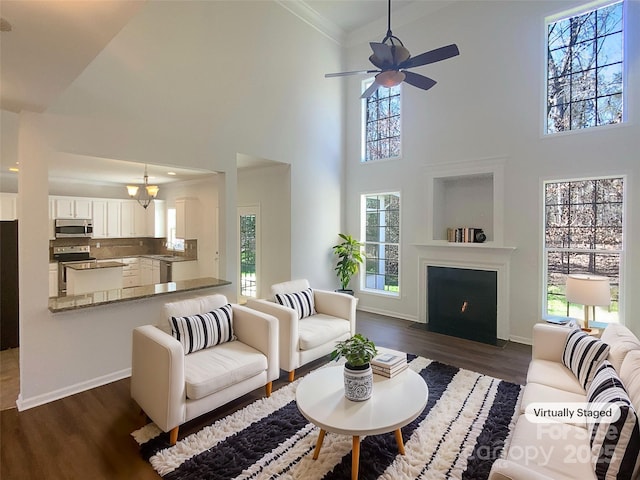 living room featuring baseboards, dark wood-type flooring, ornamental molding, and a ceiling fan