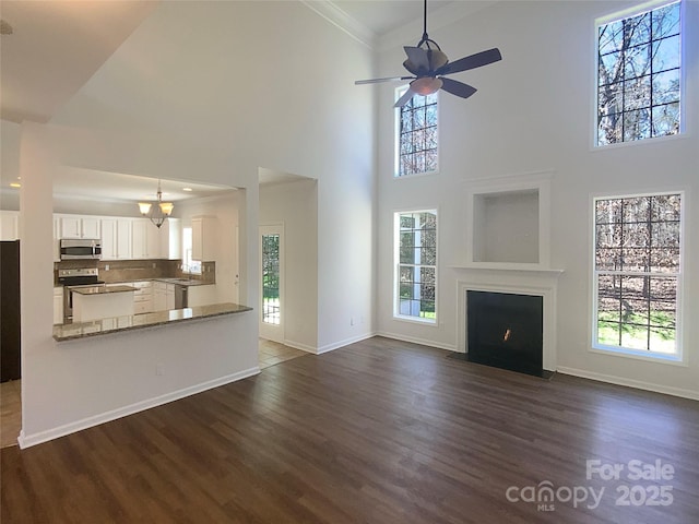 unfurnished living room featuring ceiling fan, baseboards, dark wood-style floors, and a fireplace with flush hearth