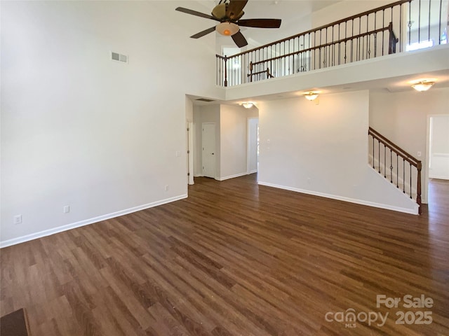 unfurnished living room featuring baseboards, visible vents, dark wood-style flooring, ceiling fan, and stairs