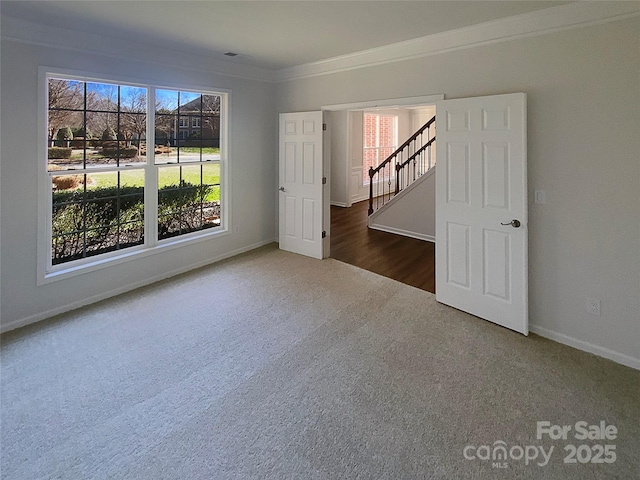 carpeted spare room featuring stairway, baseboards, and ornamental molding