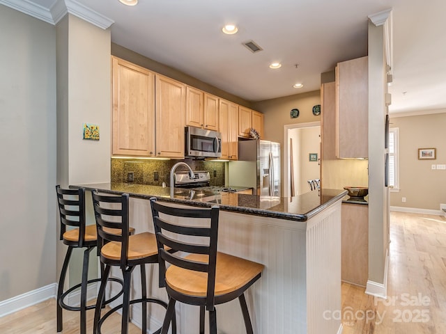kitchen featuring backsplash, a peninsula, stainless steel appliances, light brown cabinets, and visible vents