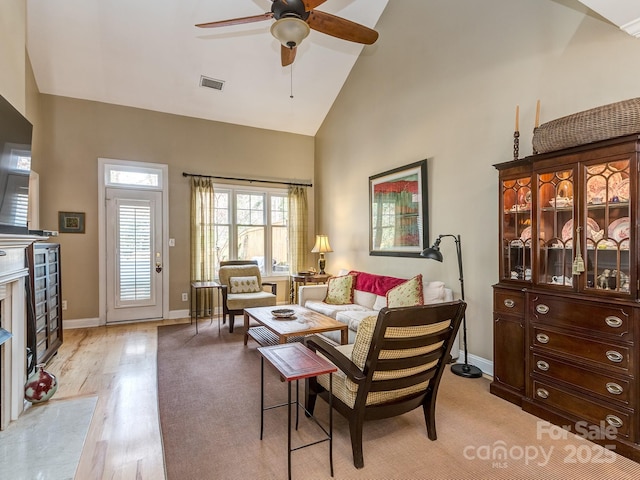 living room with high vaulted ceiling, light wood-type flooring, baseboards, visible vents, and ceiling fan