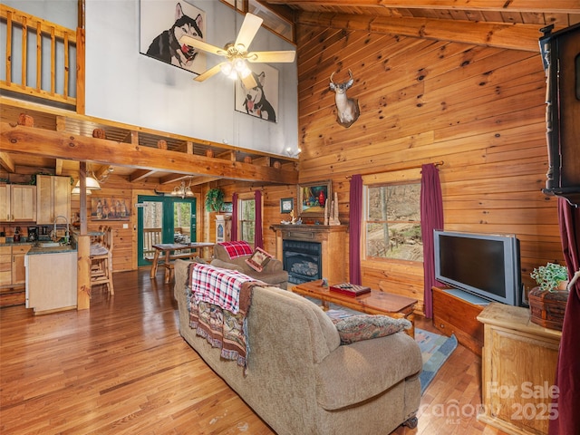 living area with ceiling fan, wooden walls, lofted ceiling with beams, and light wood-style flooring
