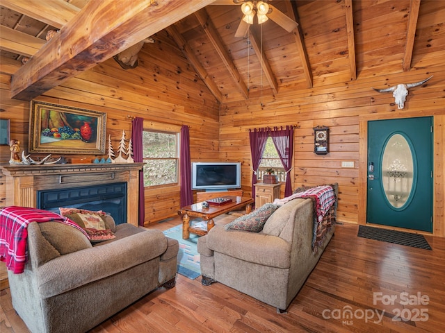 living area featuring wooden walls, beamed ceiling, wood ceiling, wood finished floors, and a glass covered fireplace