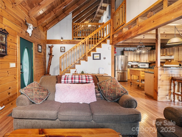 living room featuring light wood finished floors, wood walls, stairs, beam ceiling, and high vaulted ceiling