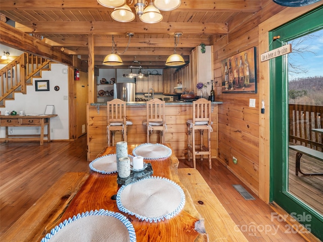 dining room featuring visible vents, a chandelier, wood walls, beam ceiling, and light wood-style flooring