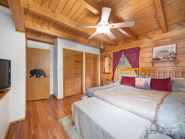 bedroom with wooden walls, two closets, baseboards, wooden ceiling, and wood-type flooring