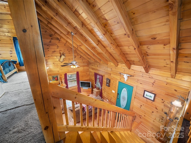 stairs with beam ceiling, wood walls, wooden ceiling, and a ceiling fan