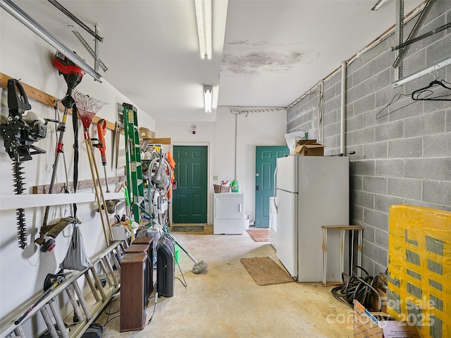 garage featuring washer / clothes dryer, concrete block wall, and freestanding refrigerator