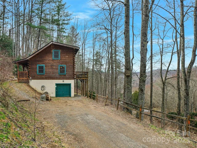 view of side of home featuring log siding, a garage, dirt driveway, and a wooden deck