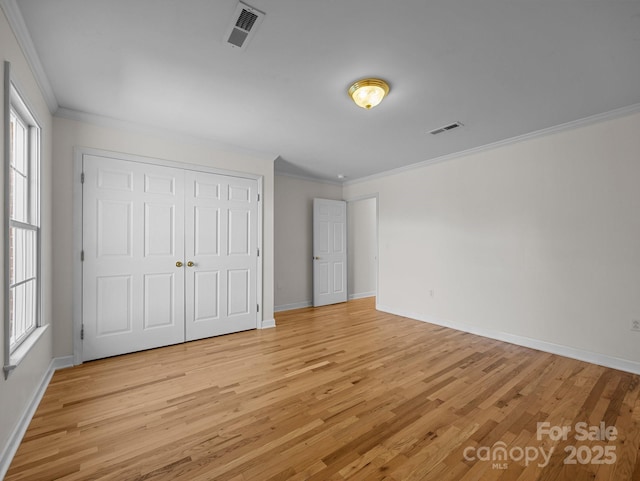 unfurnished bedroom featuring crown molding, light wood-style floors, visible vents, and a closet