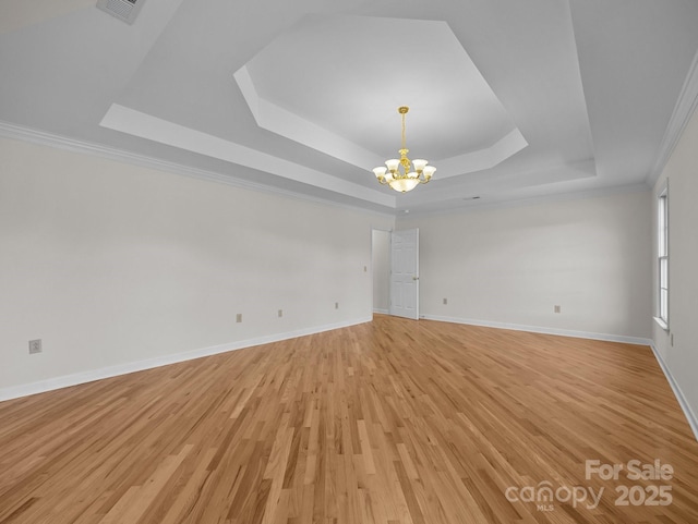 empty room featuring visible vents, baseboards, light wood-style flooring, an inviting chandelier, and a raised ceiling