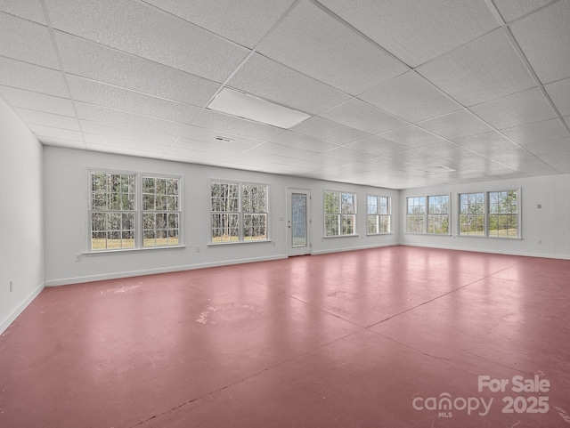 unfurnished living room with a drop ceiling, baseboards, and concrete flooring