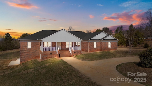 view of front of property with a porch, brick siding, a front yard, and curved driveway