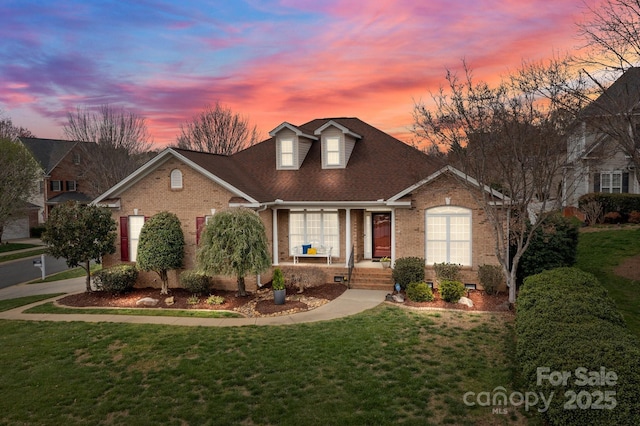 view of front of home featuring brick siding, roof with shingles, and a front yard