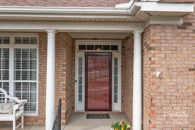 doorway to property featuring brick siding and roof with shingles