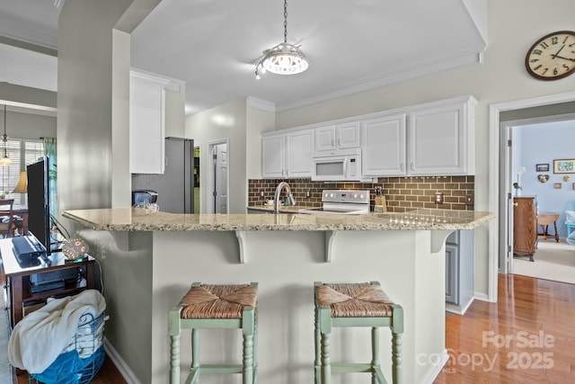 kitchen with white appliances, light stone countertops, a breakfast bar, white cabinetry, and backsplash