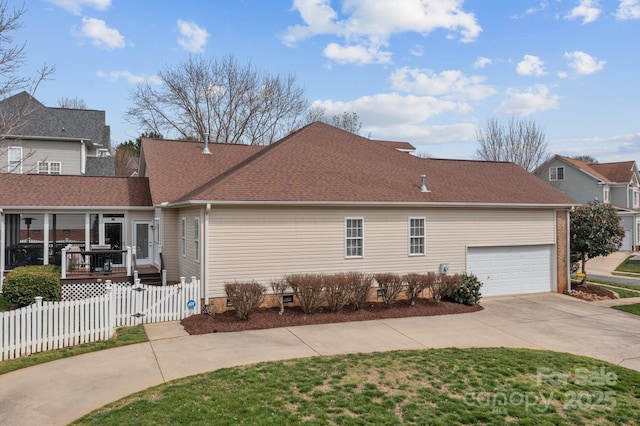 view of property exterior with roof with shingles, concrete driveway, an attached garage, and fence