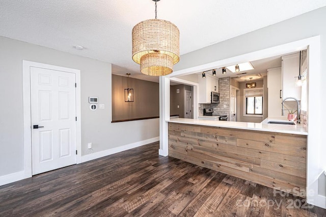 kitchen featuring dark wood-type flooring, a notable chandelier, a sink, stainless steel appliances, and baseboards