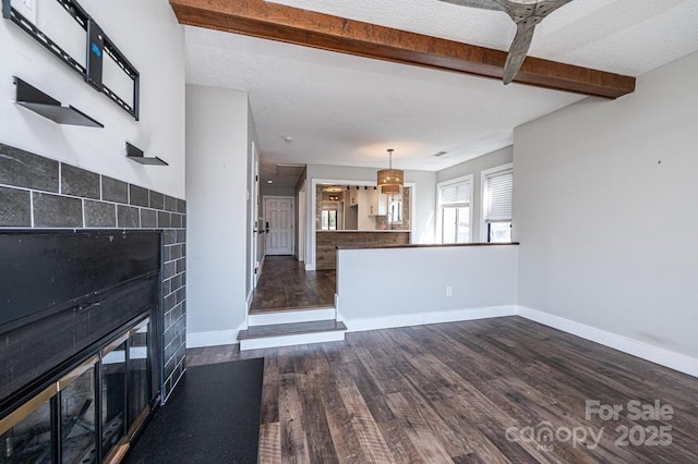 unfurnished living room featuring wood finished floors, baseboards, beam ceiling, a fireplace, and a textured ceiling