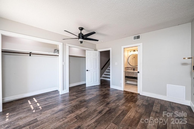 unfurnished bedroom featuring wood finished floors, visible vents, two closets, and baseboards