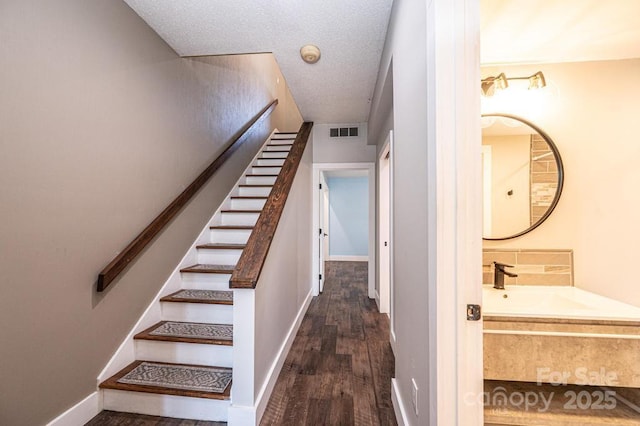 stairway featuring visible vents, baseboards, a textured ceiling, and wood finished floors