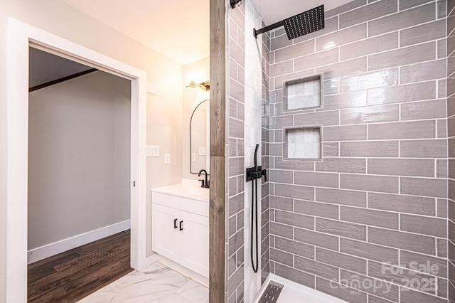 bathroom with vanity, baseboards, marble finish floor, and tiled shower