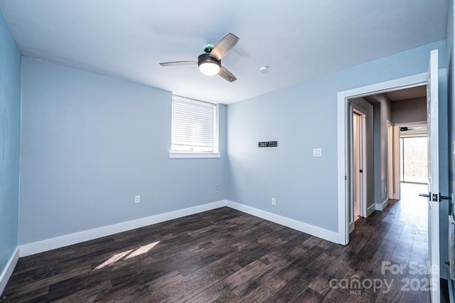 unfurnished room featuring a wealth of natural light, dark wood finished floors, baseboards, and ceiling fan