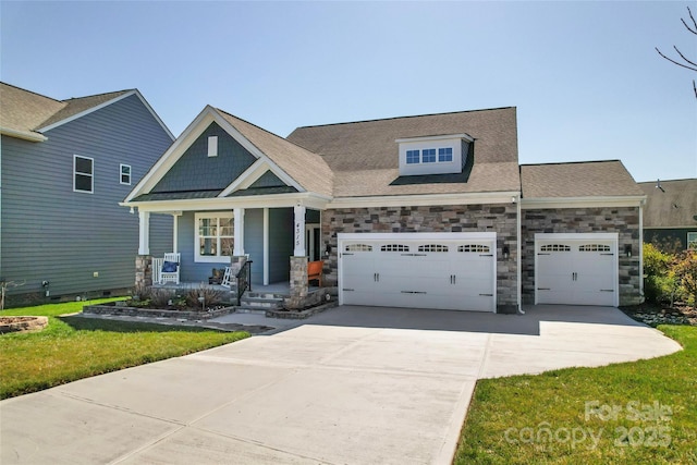 craftsman house featuring a front lawn, stone siding, covered porch, concrete driveway, and an attached garage