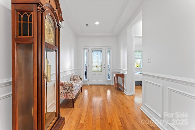 foyer featuring recessed lighting, a decorative wall, wainscoting, light wood finished floors, and a raised ceiling