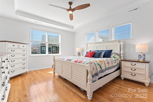 bedroom featuring light wood finished floors, visible vents, a raised ceiling, and baseboards