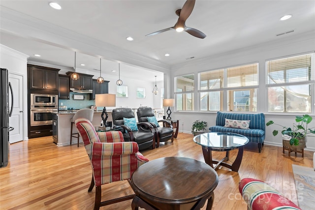 living area featuring light wood-type flooring, visible vents, ornamental molding, a ceiling fan, and baseboards