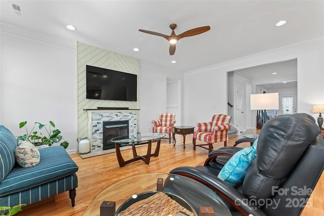 living area with wood finished floors, a fireplace, ceiling fan, and crown molding