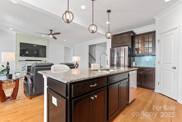 kitchen with a ceiling fan, light wood finished floors, a sink, stainless steel appliances, and backsplash