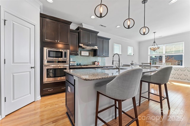 kitchen with visible vents, a breakfast bar, a sink, stone countertops, and stainless steel appliances