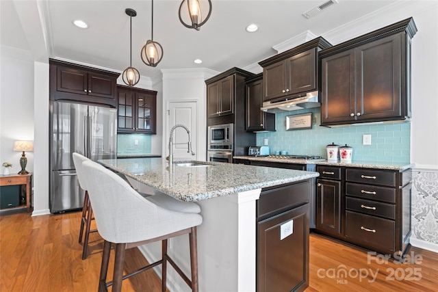 kitchen with visible vents, under cabinet range hood, appliances with stainless steel finishes, light wood-style floors, and a sink