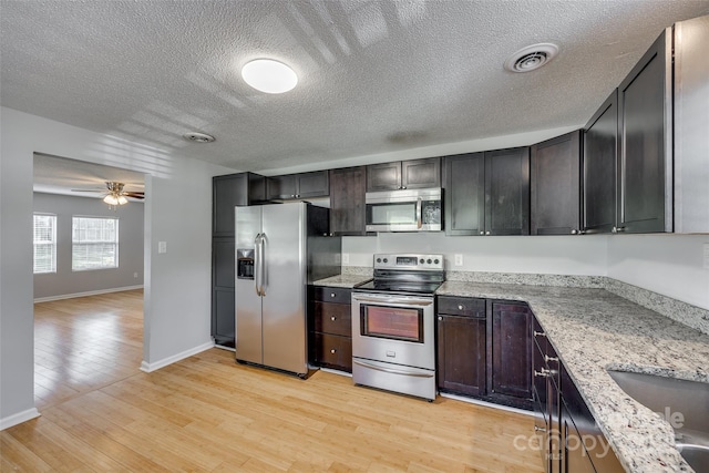 kitchen with visible vents, a ceiling fan, stainless steel appliances, light wood finished floors, and light stone countertops