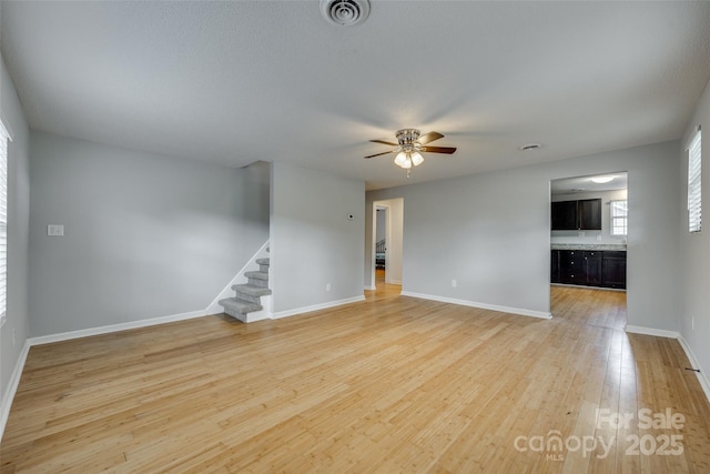 unfurnished living room featuring baseboards, visible vents, ceiling fan, stairs, and light wood-style floors