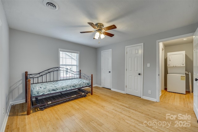 bedroom with visible vents, baseboards, stacked washer and dryer, and wood finished floors