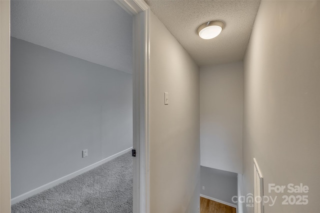 hallway featuring carpet flooring, a textured ceiling, and baseboards