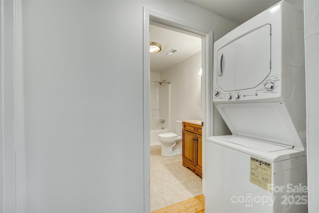 laundry room featuring light tile patterned floors, visible vents, stacked washer and dryer, and laundry area